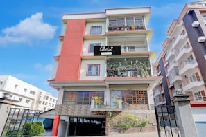Un edificio residencial de varios pisos con letrero de empresa, balcones con plantas en macetas y entrada a un garaje.