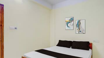 Un dormitorio con una cama, dos cuadros en la pared y un enchufe.