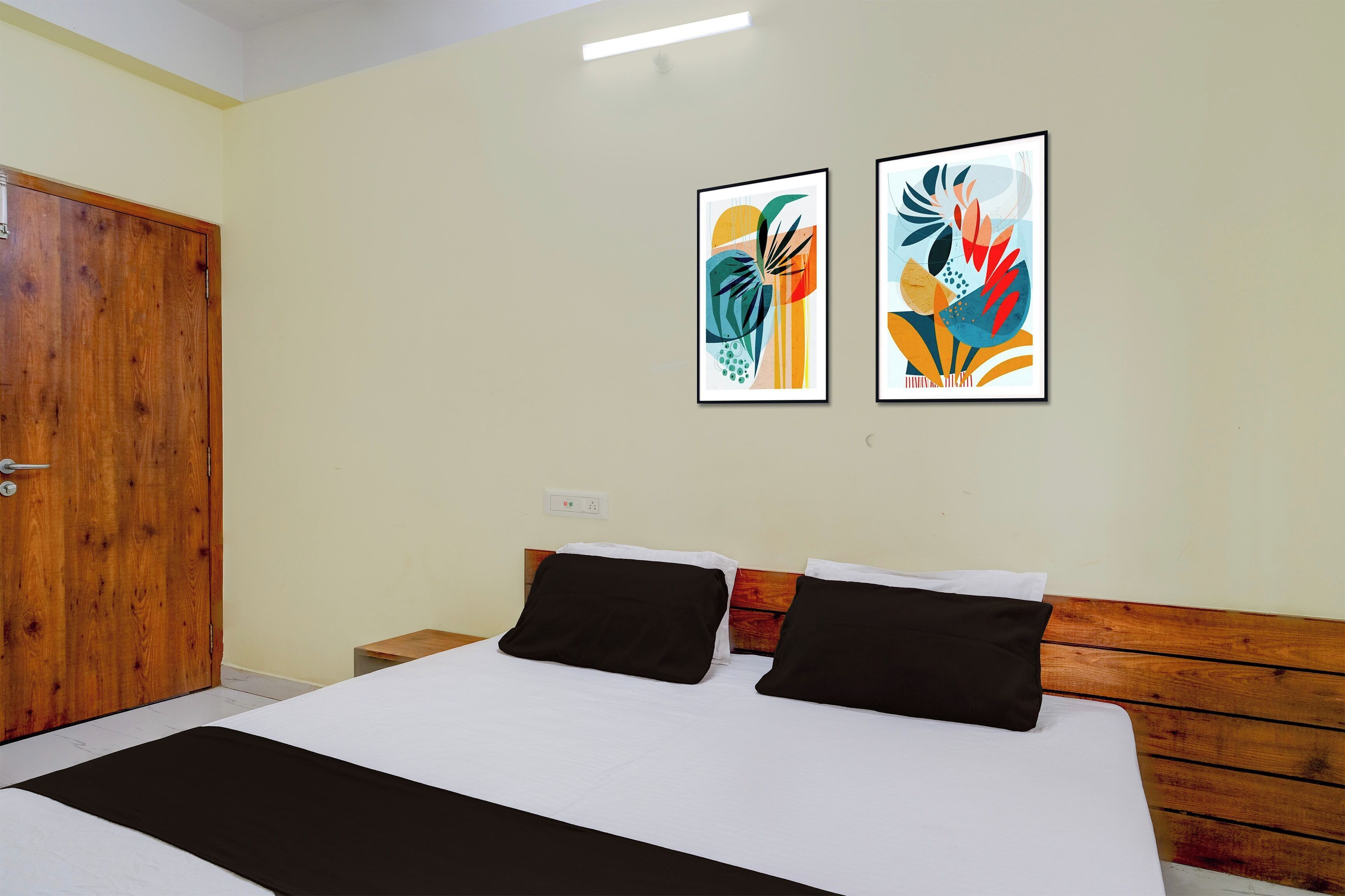 Ein Hotelzimmer mit Holztür, einem Bett mit weiß-schwarzer Bettwäsche und zwei abstrakten Bildern an der Wand.