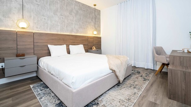 Ein modernes Schlafzimmer mit einem großen Bett, Nachttischen, einem Schreibtisch und einem großen Fenster mit Vorhängen.