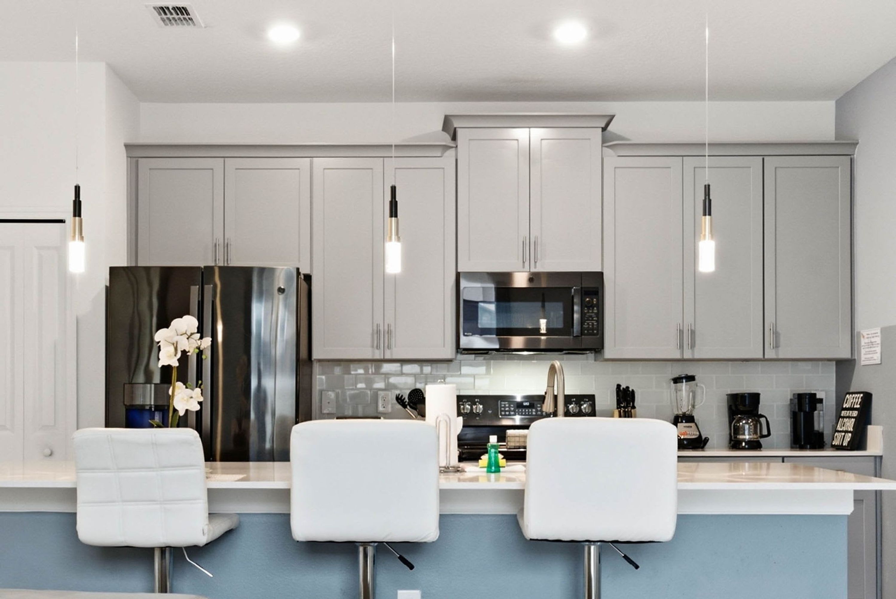 A modern kitchen with grey cabinets, stainless steel appliances, and pendant lighting.