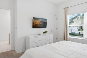 Ein Schlafzimmer mit einem Bett, einer Kommode, einem Bild und einem Fenster mit Blick auf ein Gebäude.