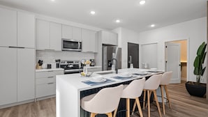 A modern kitchen with white cabinetry, a central island with bar stools, a microwave, a refrigerator, and a sink. - Chic Home Just 15 Min to Disney (Davenport)