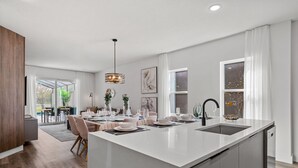 A modern kitchen with a large island, white cabinetry, and a built-in dishwasher. - Chic Home Just 15 Min to Disney (Davenport)