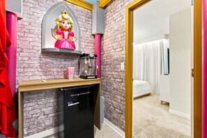 Ein Zimmer mit Backsteinwand, einem Bett mit weißen Vorhängen, einem kleinen Schreibtisch mit Kaffeemaschine und einem Kühlschrank.