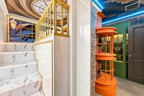 Eine Treppe mit Marmorstufen und einer goldenen Gitterspindel, ein spiralförmiges, oranges Bücherregal und eine Decke mit Sternenmuster.