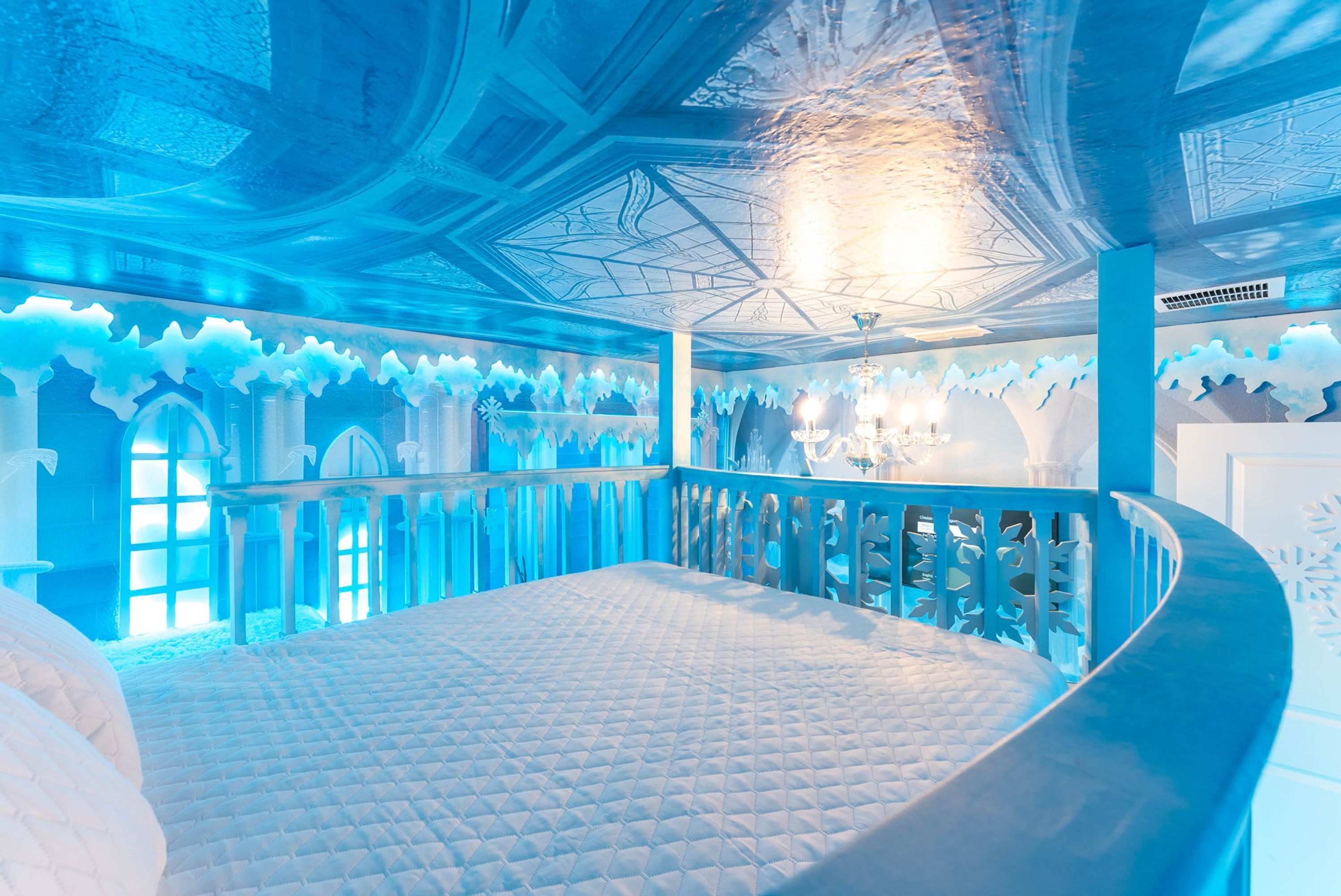 A room with a curved balcony, a bed with a quilted mattress, and a chandelier.