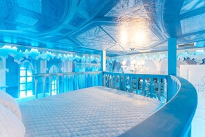 Ein Zimmer mit einem gebogenen Balkon, einem Bett mit gesteppter Matratze und einem Chandelier.
