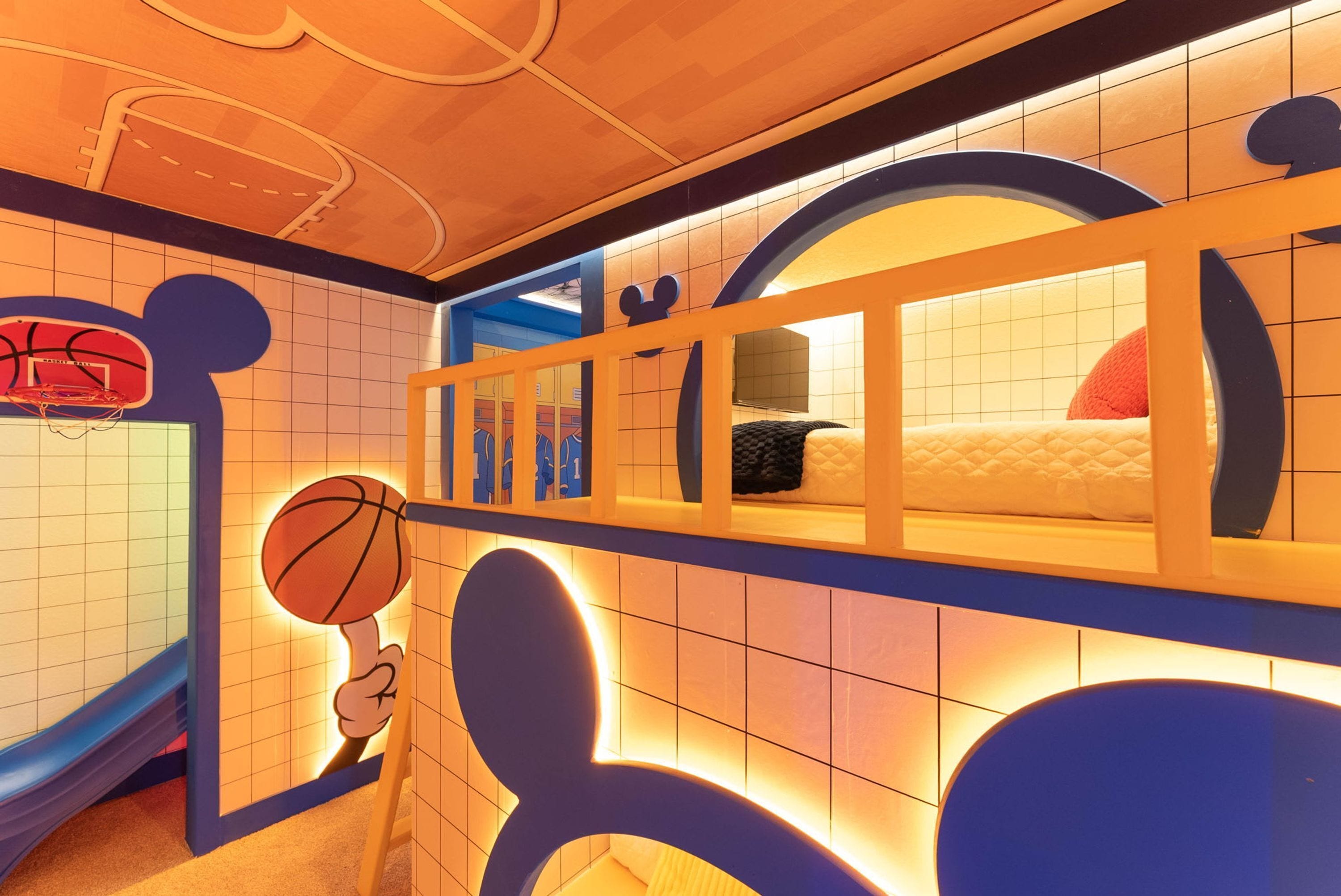 A children's play area with a basketball hoop, a slide, and a window with a bed and pillows.