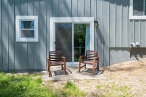 En utomhusplats med två stolar, placerad framför en byggnad med en skjutdörr i glas och ett litet fönster.