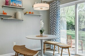 Ein modernes Interieur mit einem runden Tisch, zwei Holzstühlen, einer Pendelleuchte und einem gemusterten Vorhang.