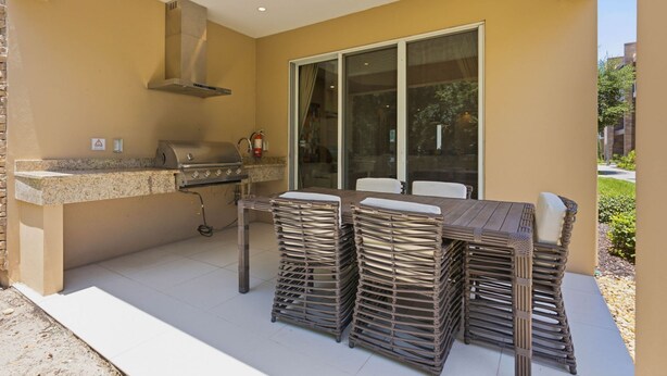 An outdoor kitchen area with a grill, a chimney, and a table with stacked chairs. - Stylish 4 Ensuite Home Near Disney Free BBQ Grill (Kissimmee)