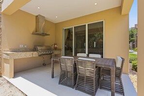 Un área de cocina exterior con una parrilla, una chimenea y una mesa con sillas apiladas.