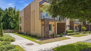 A modern multi-story residential building with a stone facade, a covered balcony, and a well-maintained lawn. - Stylish 4 Ensuite Home Near Disney Free BBQ Grill (Kissimmee)