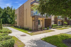 A modern multi-story residential building with a stone facade, a covered balcony, and a well-maintained lawn. - Stylish 4 Ensuite Home Near Disney Free BBQ Grill (Kissimmee)