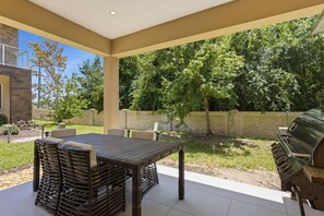 An outdoor patio with a table and chairs, a grill, and a stone wall. - Stylish 4 Ensuite Home Near Disney Free BBQ Grill (Kissimmee)