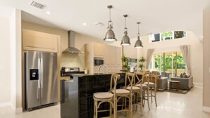 A modern kitchen with a stainless steel refrigerator, a black marble island, and wooden chairs. - Stylish 4 Ensuite Home Near Disney Free BBQ Grill (Kissimmee)
