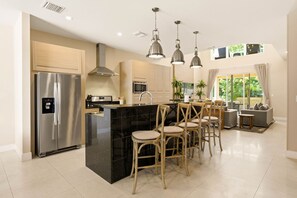 A modern kitchen with a stainless steel refrigerator, a black marble island, and wooden chairs. - Stylish 4 Ensuite Home Near Disney Free BBQ Grill (Kissimmee)