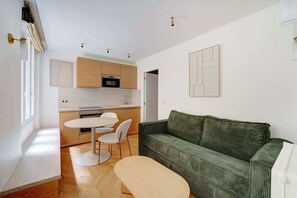 Eine moderne Küche mit Holzausbau, einem Esstisch mit Stühlen und einem grünen Sofa im Wohnbereich.