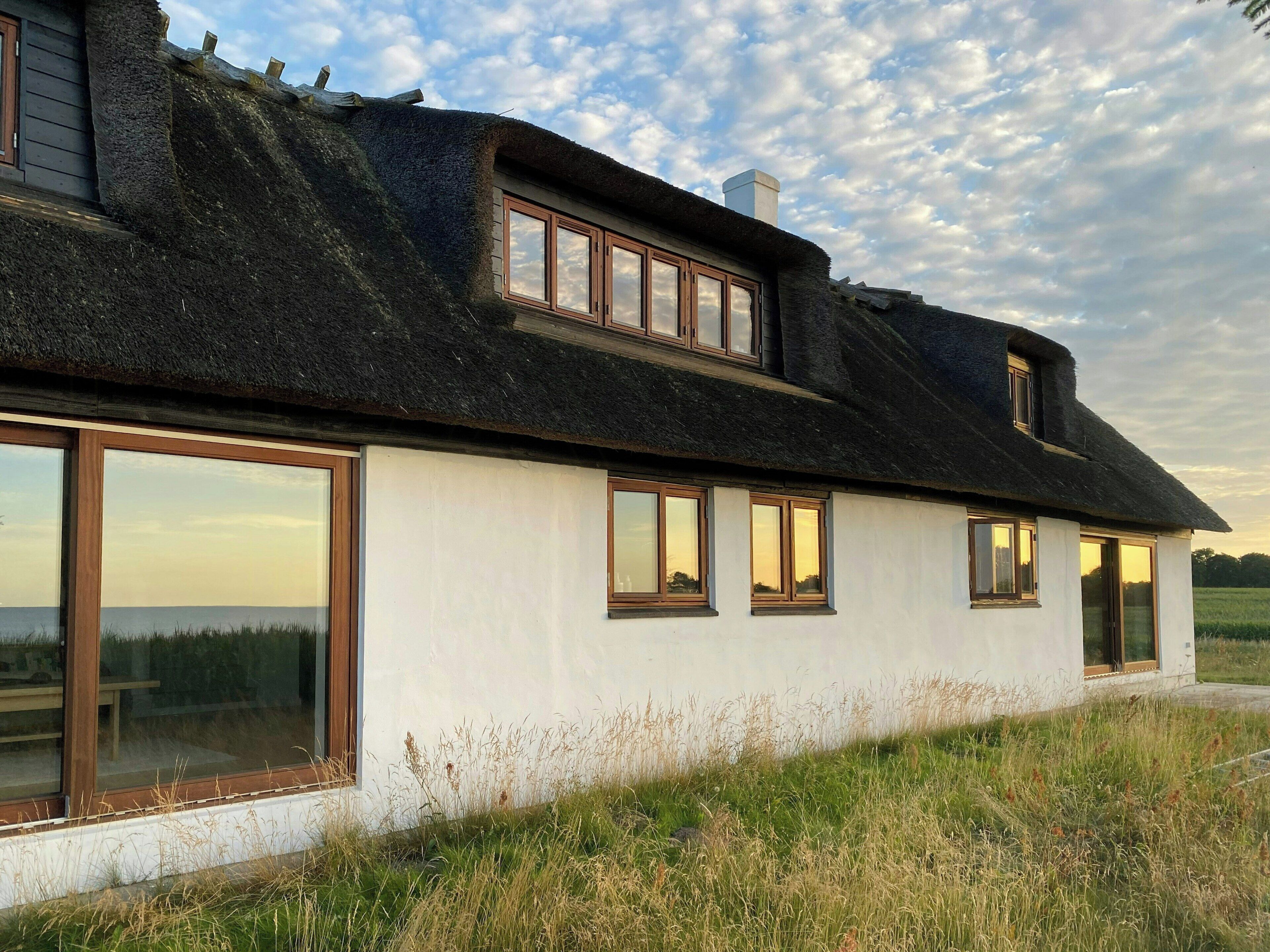 Een huis met rieten dak, grote ramen en een gazon op de voorgrond.
