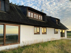 Ein Haus mit einem Strohdach, großen Fenstern und einem Rasen im Vordergrund.