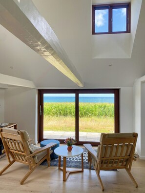 Et værelse med en stor skydedør, der giver udsigt over havet, møbler af træ og et lille bord med en vase.