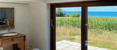 A room with a wooden table, chairs, a sofa, and a view of the sea through a glass door.