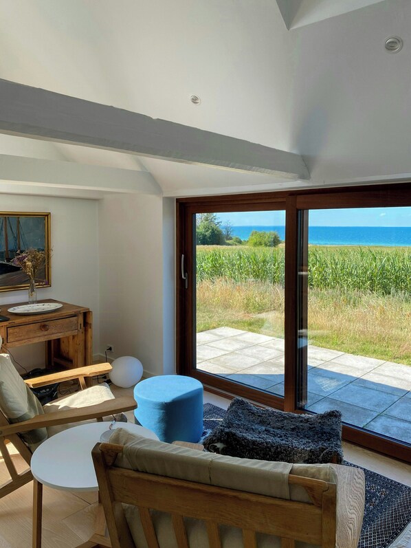 A room with a wooden table, chairs, a sofa, and a view of the sea through a glass door. - Fisherman's cottage from 1873 near Bønnerup (Allingåbro)