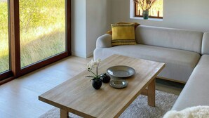 Ett modernt vardagsrum med en soffa, ett soffbord och utsikt över ett vackert naturlandskap genom stora fönster.