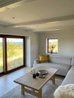 Ein modernes Wohnzimmer mit einer Couch, einem Couchtisch und Blick auf eine natürliche Landschaft durch große Fenster.