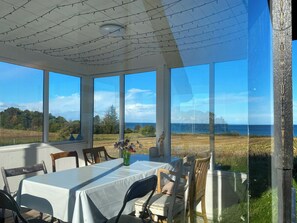 A covered outdoor dining area with a table and chairs, large windows, and a view of the sea. - Fisherman's cottage from 1873 near Bønnerup (Allingåbro)