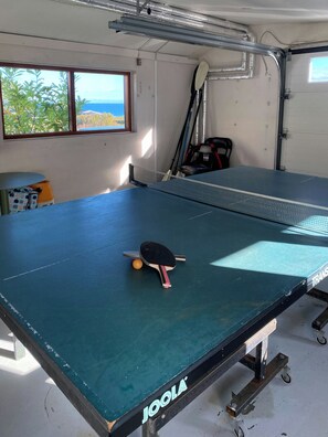 Ett bordtennisbord med ett racket, ett fönster med utsikt och en stol.