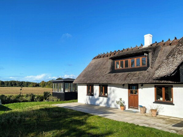 Et traditionelt hus med stråtækt tag, hvid facade, en trædør og et vindue med trærammer.