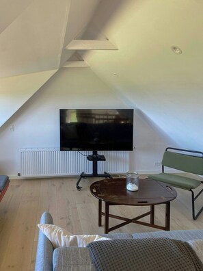 A living room with a flat-screen TV mounted on a stand, a wooden coffee table, a green chair, and a sofa with cushions. - Fisherman's cottage from 1873 near Bønnerup (Allingåbro)