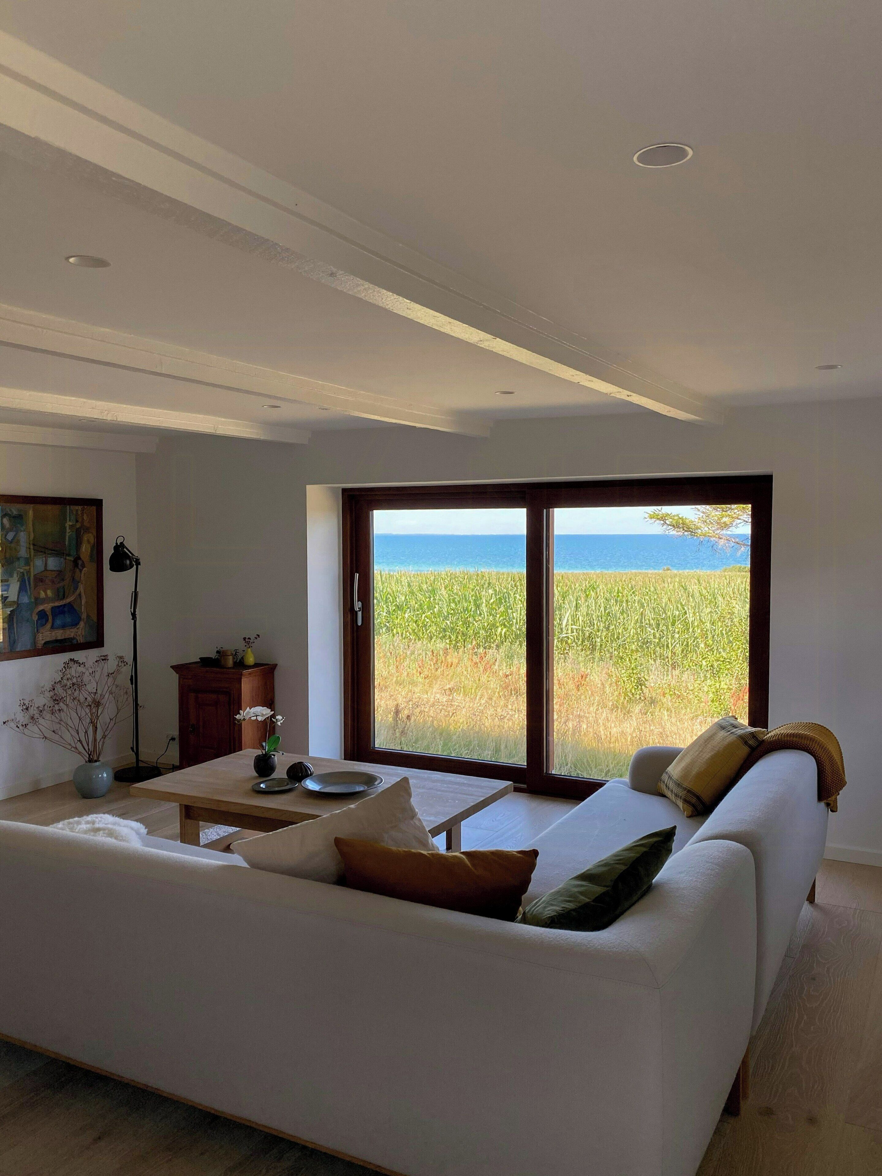 A living room with a white sofa, a dining table, and a view of the ocean through large glass doors.