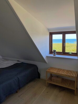 Une chambre avec un lit, un petit banc en bois, une fenêtre donnant sur la mer et un plafond en pente.