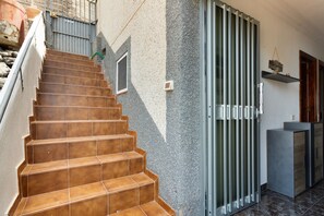 Un escalier recouvert de carreaux bruns mène à une porte surmontée d’un portail en métal.