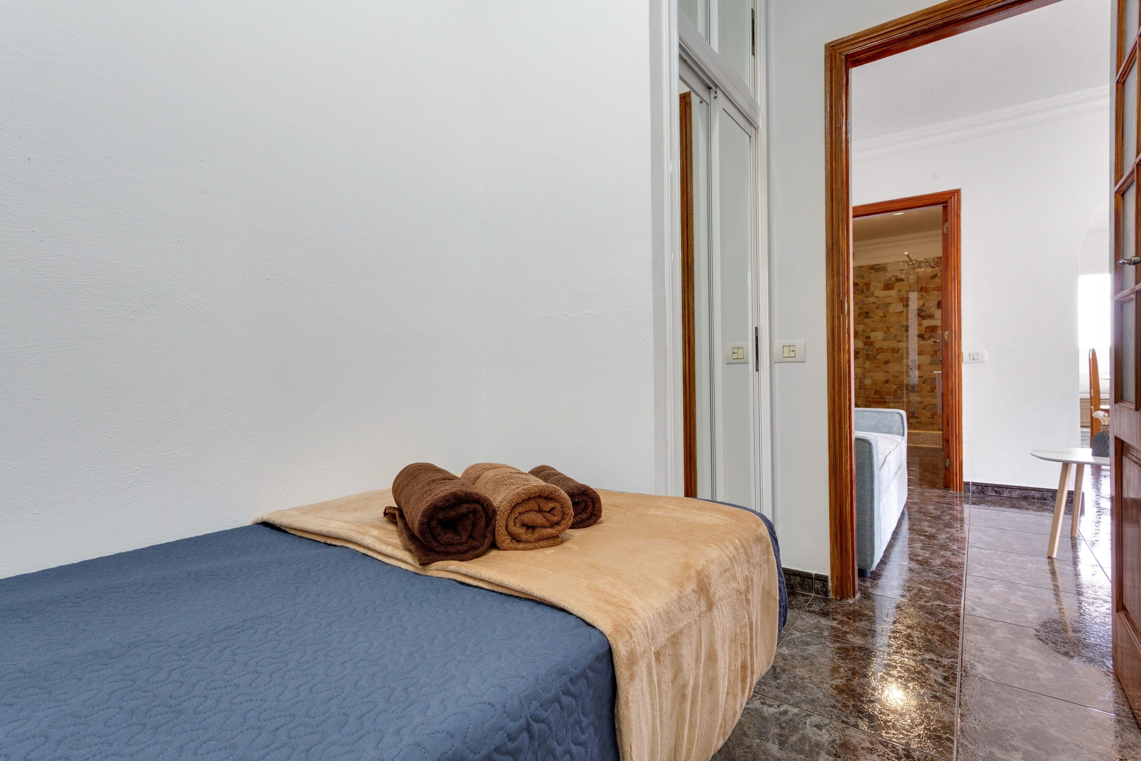 A hotel room with a bed, a bathroom visible through an open door, and a shower area with a stone wall.