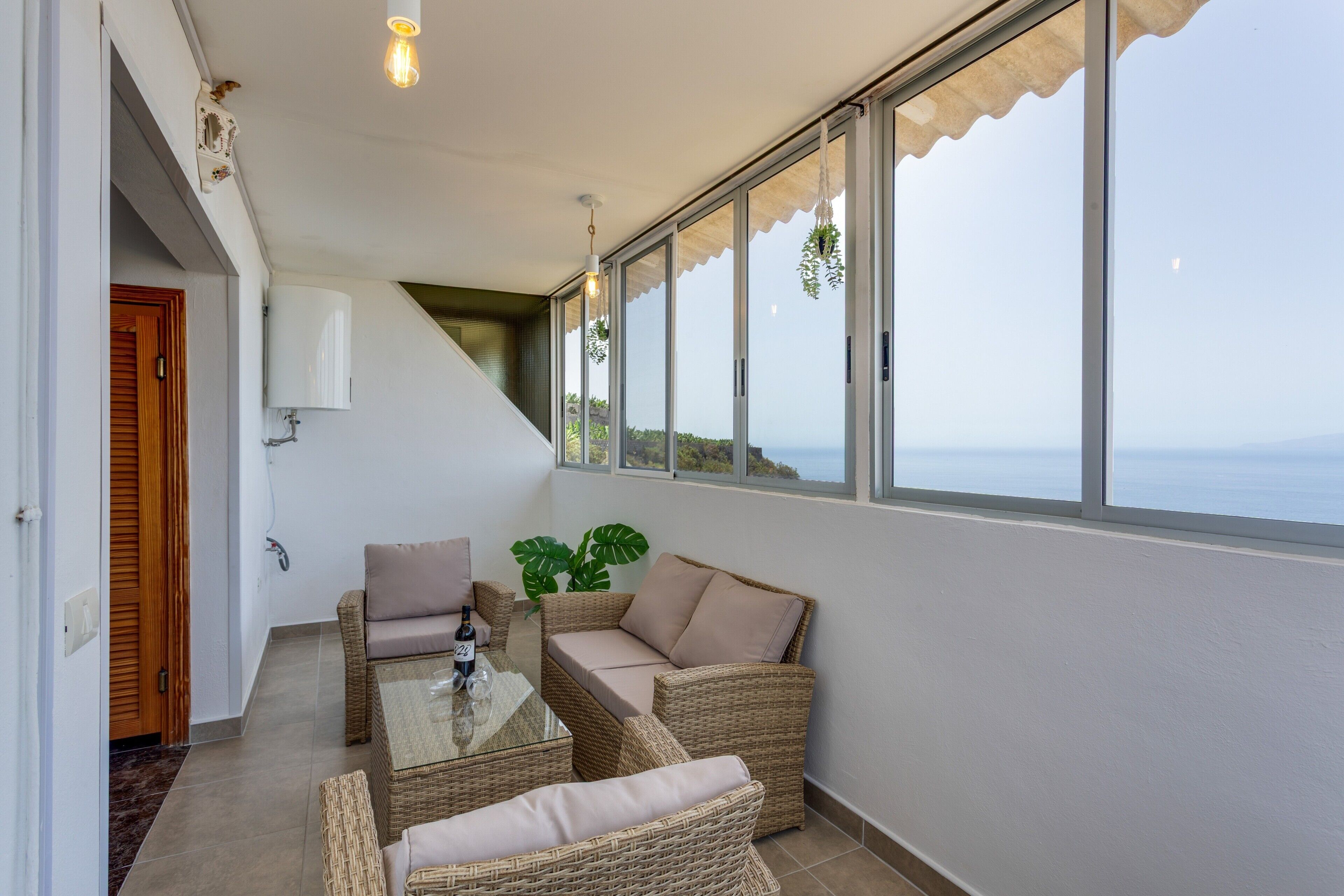 A balcony with wicker furniture, a glass table, and a view of the sea.