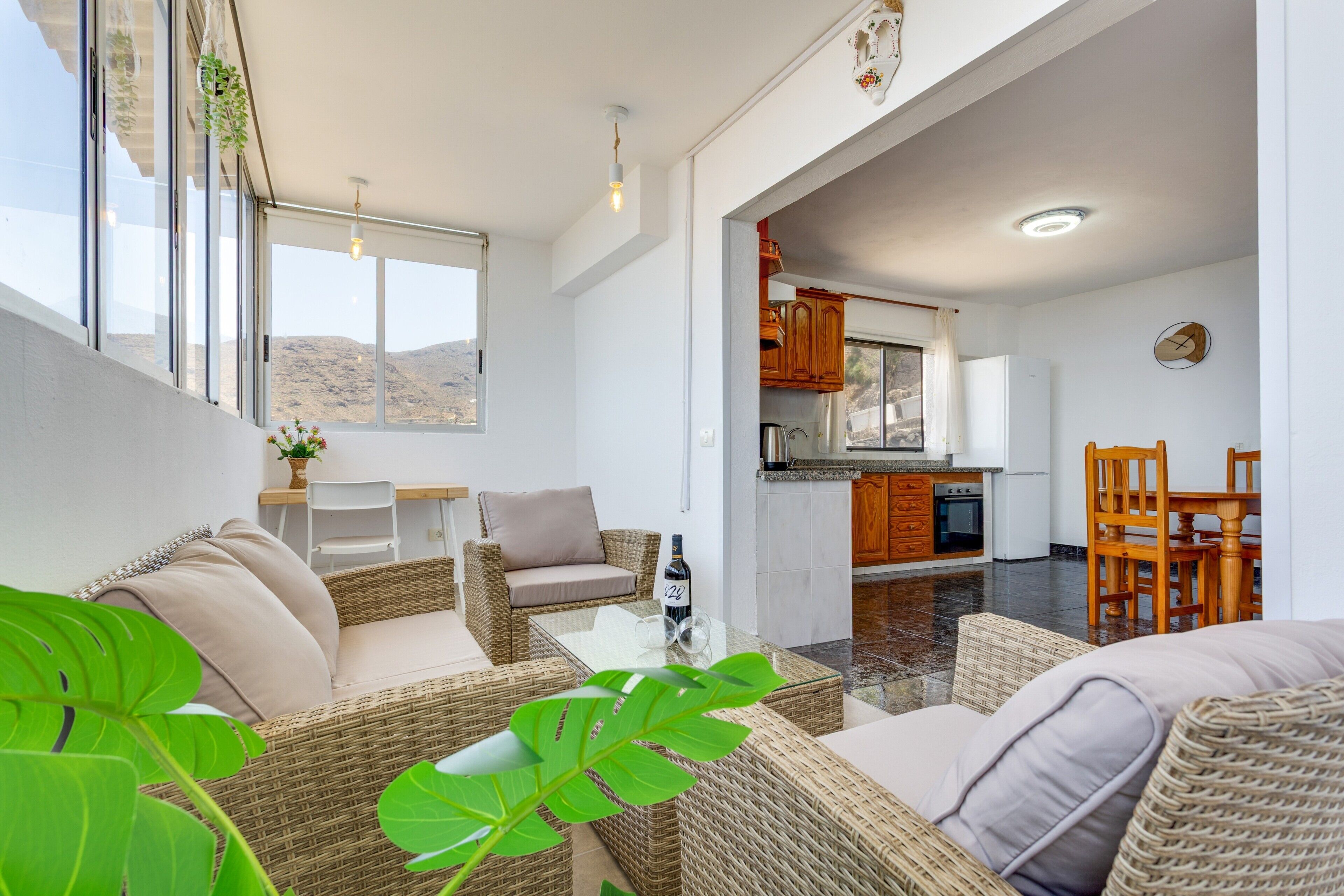 A modern living room with wicker furniture, a dining area with wooden chairs, and a kitchen with wooden cabinets.