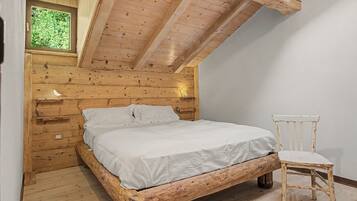 Une chambre à coucher en bois avec un plafond en pente, un lit, une table de chevet, une chaise et une fenêtre.