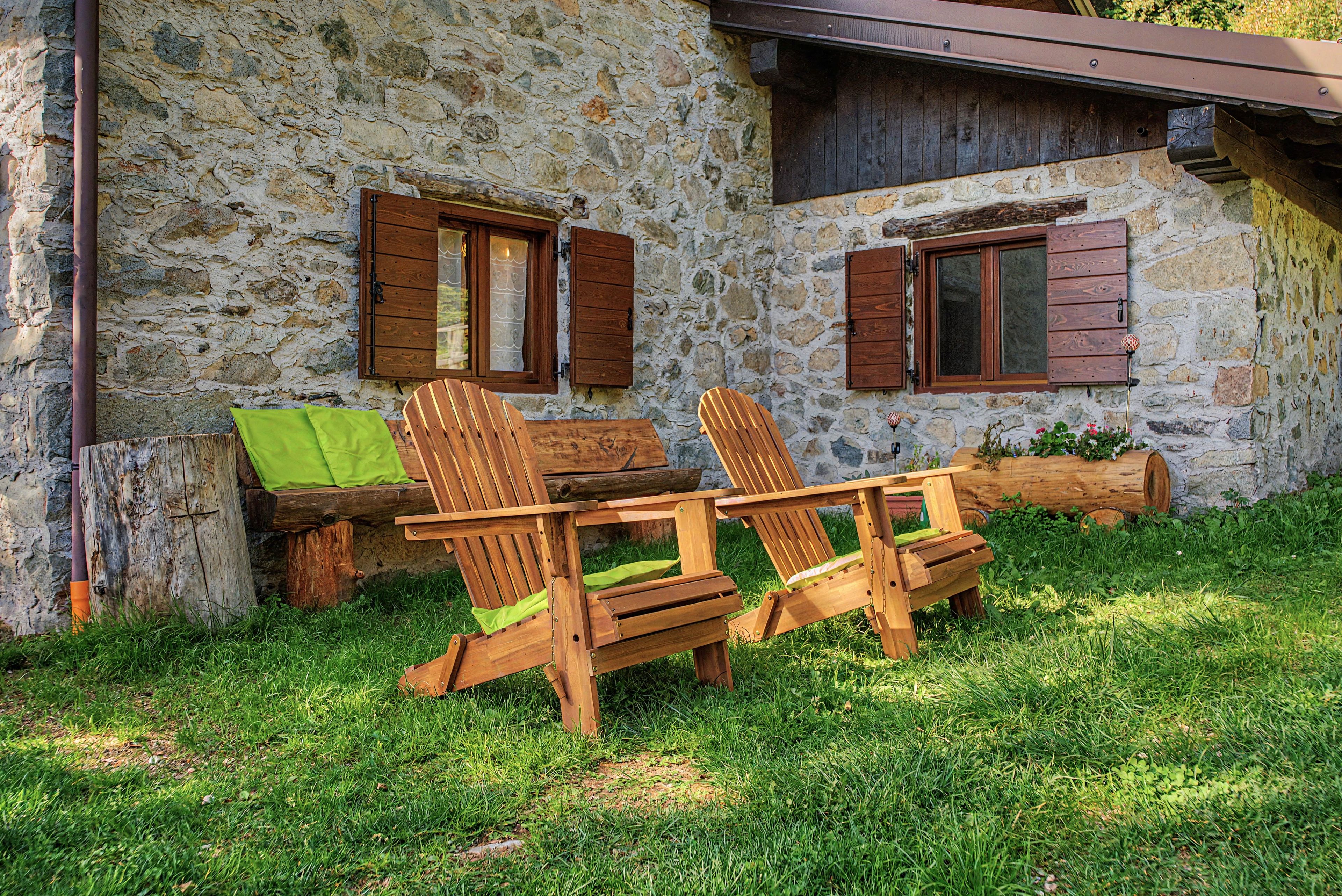 Un edificio de piedra con contraventanas de madera, una mesa de madera con sillas y un área con césped.