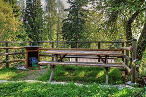 Una mesa de picnic de madera con bancos, rodeada por una valla de madera, ubicada en una zona boscosa.
