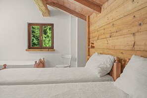 Ein Zimmer mit zwei Betten, einem Fenster mit Blick auf Grünflächen und Holzwänden.