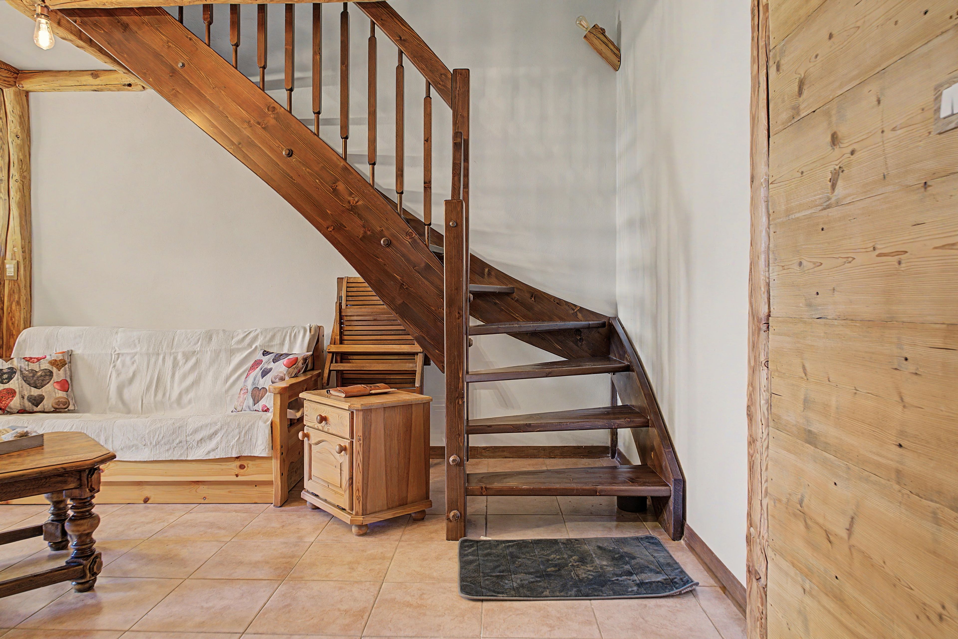 Un escalier en bois, un meuble en bois et un canapé dans une pièce dont le sol est recouvert de carreaux.