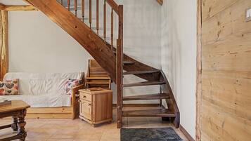 Un escalier en bois, un meuble en bois et un canapé dans une pièce dont le sol est recouvert de carreaux.