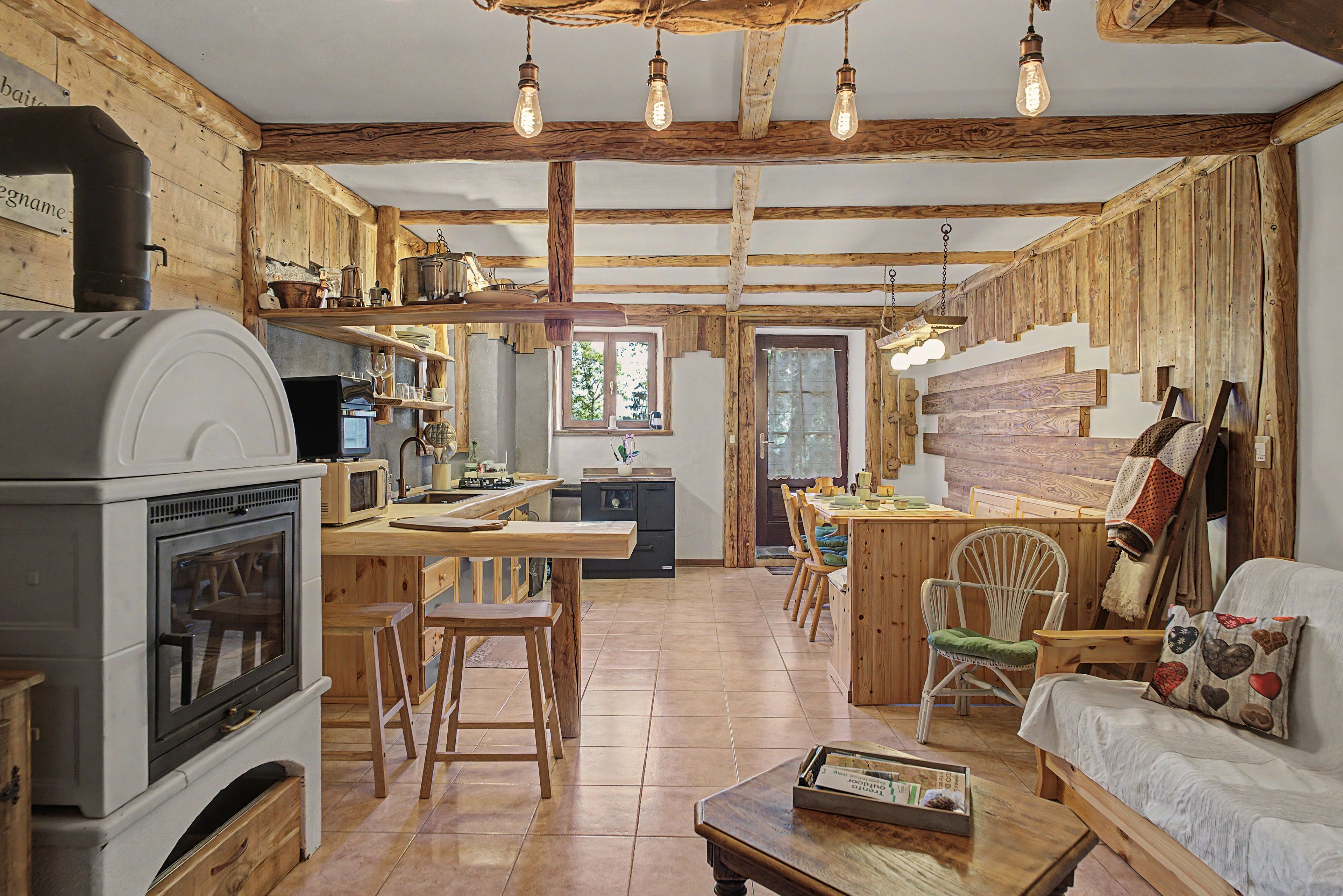 Une cuisine rustique avec un poêle à bois, des poutres apparentes et un coin repas comprenant une table et des chaises en bois.
