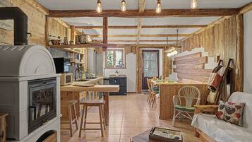 Une cuisine rustique avec un poêle à bois, des poutres apparentes et un coin repas comprenant une table et des chaises en bois.