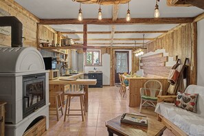 A rustic kitchen with a wood stove, wooden beams, and a dining area with a wooden table and chairs.