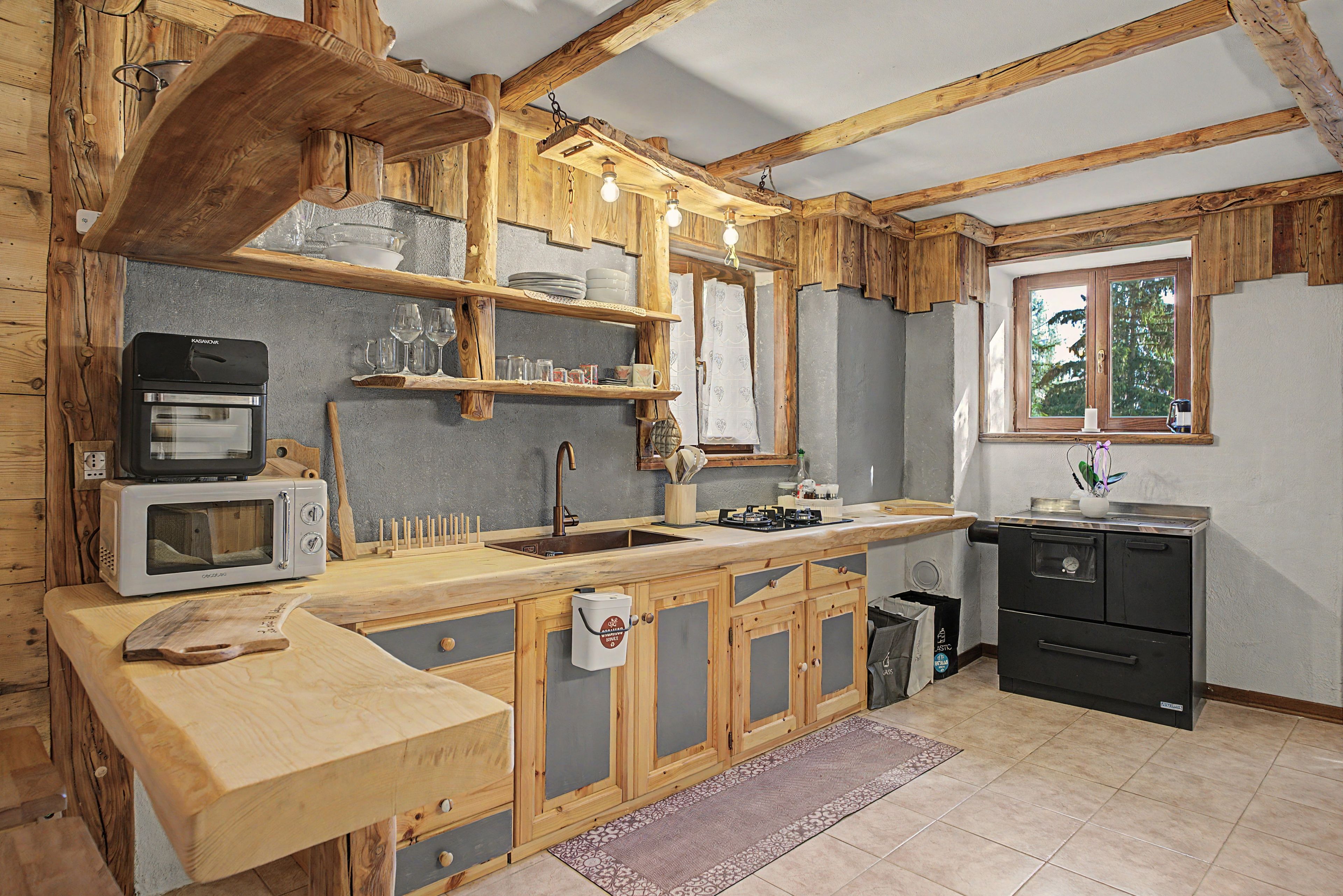 A rustic kitchen with wooden beams, a sink, a stove, and a microwave.